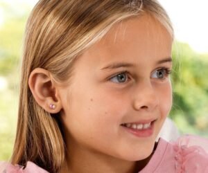 Young girl with light brown hair and pink earrings, smiling. Features bright eyes and a joyful expression, showcasing the earrings.